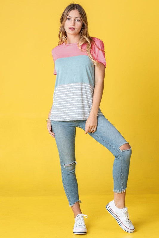 A person in a Sage Coral Black Grey Stripe Lavender Top made of polyester and jeans stands in a room with plants and white curtains.