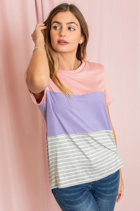 A person in a Sage Coral Black Grey Stripe Lavender Top made of polyester and jeans stands in a room with plants and white curtains.