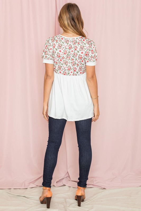 A person wearing a Baby Doll Floral Puff Sleeve Tunic and white pants stands gracefully against a pink background.