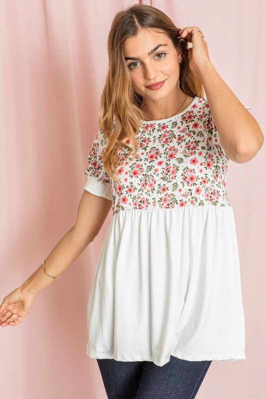 A person wearing a Baby Doll Floral Puff Sleeve Tunic and white pants stands gracefully against a pink background.