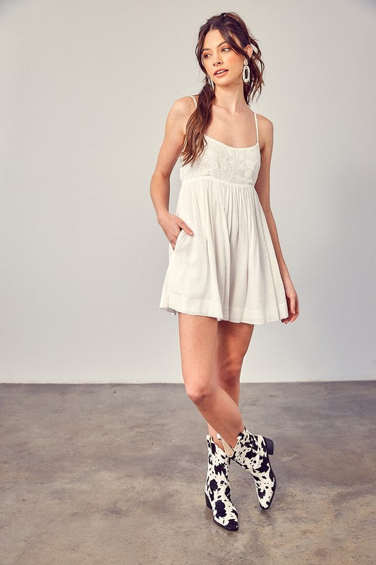 A woman wearing a Cotton Jacquard Contrast Detail Romper and contrasting cow-patterned boots strikes a pose on a concrete floor against a plain gray wall, effortlessly blending boho style with modern chic.