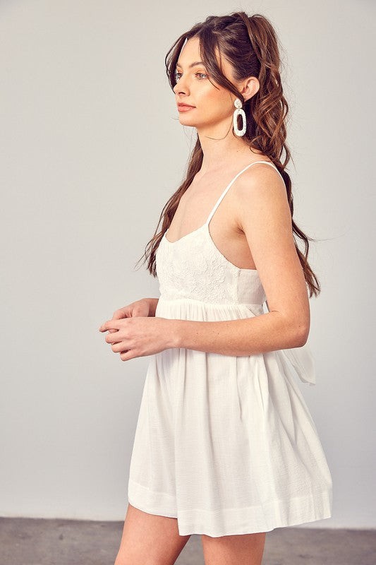 A woman wearing a Cotton Jacquard Contrast Detail Romper and contrasting cow-patterned boots strikes a pose on a concrete floor against a plain gray wall, effortlessly blending boho style with modern chic.