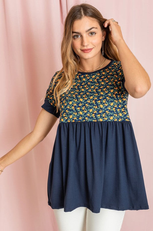 The woman stands confidently in the Plus Baby Doll Floral Puff Sleeve Tunic. Its charming puff sleeves accentuate the floral print, perfectly complementing the navy bottom half as she poses against a light pink curtain.