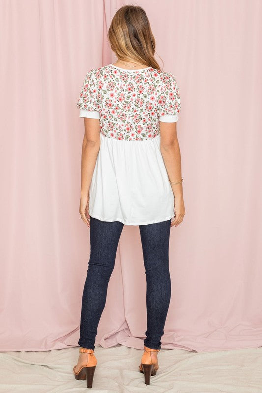 The woman stands confidently in the Plus Baby Doll Floral Puff Sleeve Tunic. Its charming puff sleeves accentuate the floral print, perfectly complementing the navy bottom half as she poses against a light pink curtain.