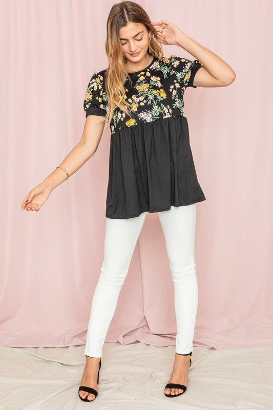 The woman stands confidently in the Plus Baby Doll Floral Puff Sleeve Tunic. Its charming puff sleeves accentuate the floral print, perfectly complementing the navy bottom half as she poses against a light pink curtain.