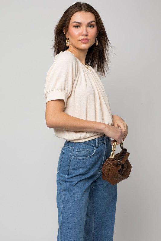 A person wearing a versatile Shirring Neck Rib Top and blue jeans holds a small brown handbag while standing against a plain background.