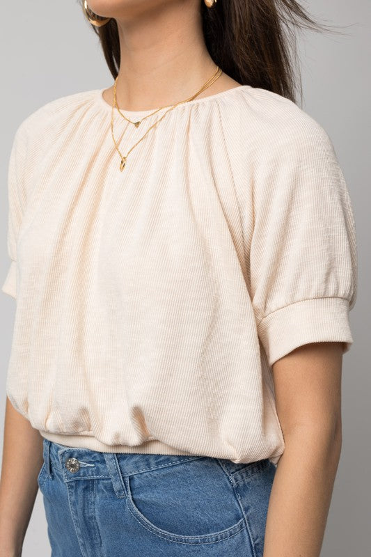 A person wearing a versatile Shirring Neck Rib Top and blue jeans holds a small brown handbag while standing against a plain background.