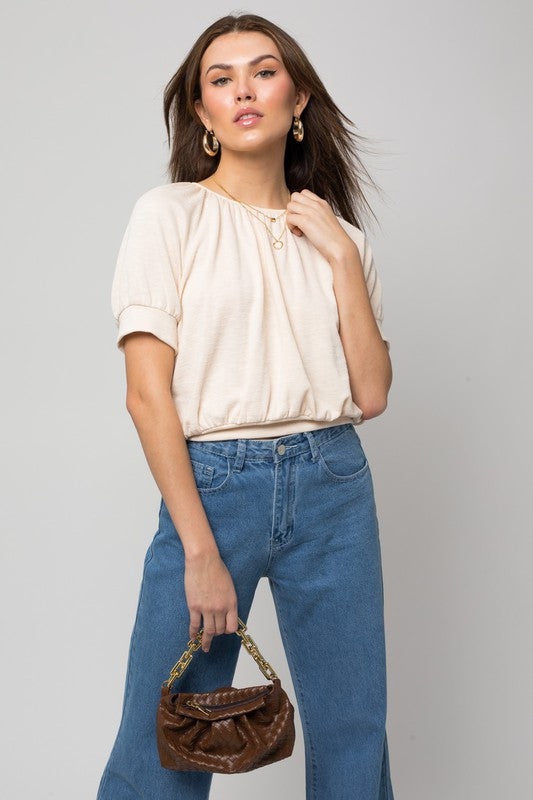 A person wearing a versatile Shirring Neck Rib Top and blue jeans holds a small brown handbag while standing against a plain background.