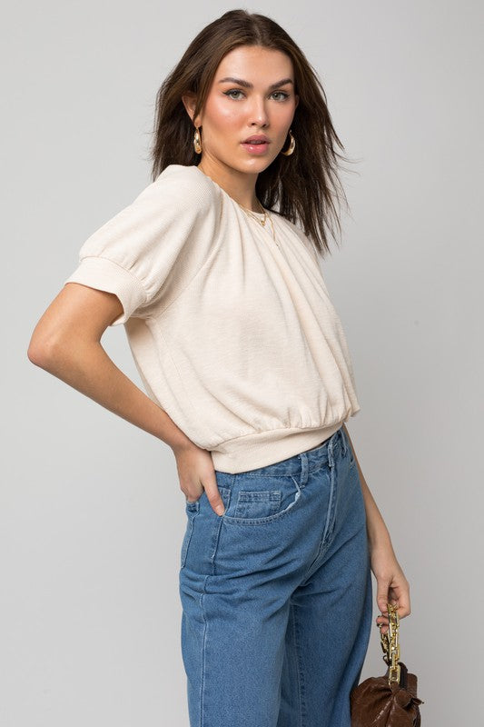 A person wearing a versatile Shirring Neck Rib Top and blue jeans holds a small brown handbag while standing against a plain background.