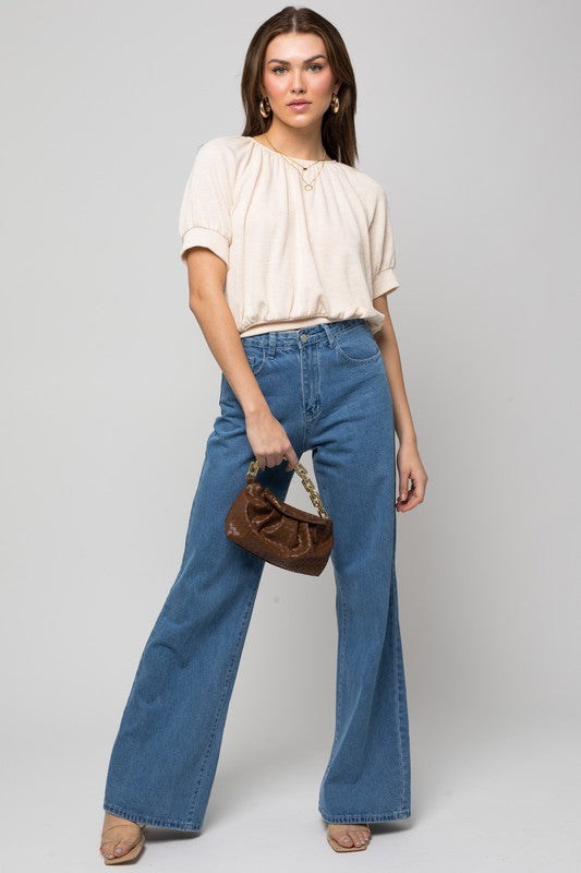 A person wearing a versatile Shirring Neck Rib Top and blue jeans holds a small brown handbag while standing against a plain background.