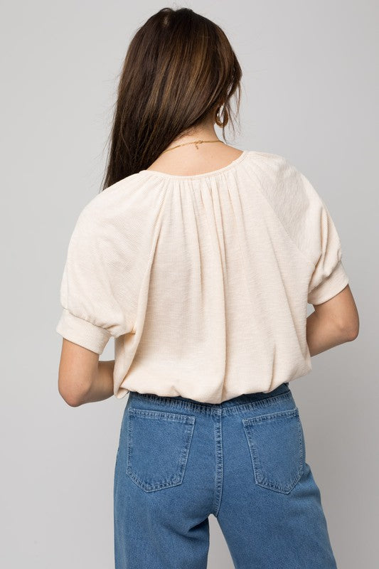 A person wearing a versatile Shirring Neck Rib Top and blue jeans holds a small brown handbag while standing against a plain background.