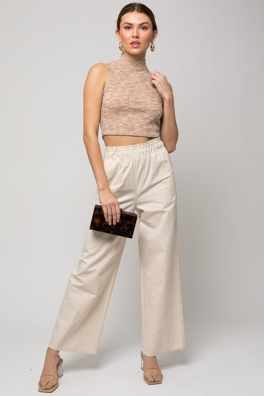 A person wearing hoop earrings, a Sleeveless Mock Neck Band Top, and high-waisted pants is holding a small clutch.