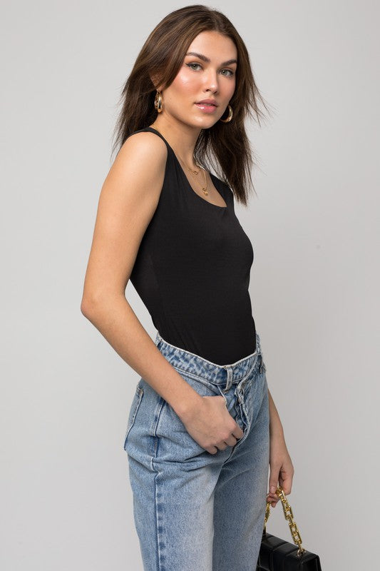 A person wearing a Cap Sleeve Square Neck Bodysuit and jeans holds a black handbag, showcasing a true fashion essential.