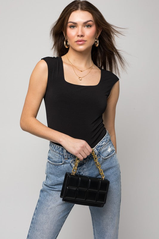 A person wearing a Cap Sleeve Square Neck Bodysuit and jeans holds a black handbag, showcasing a true fashion essential.