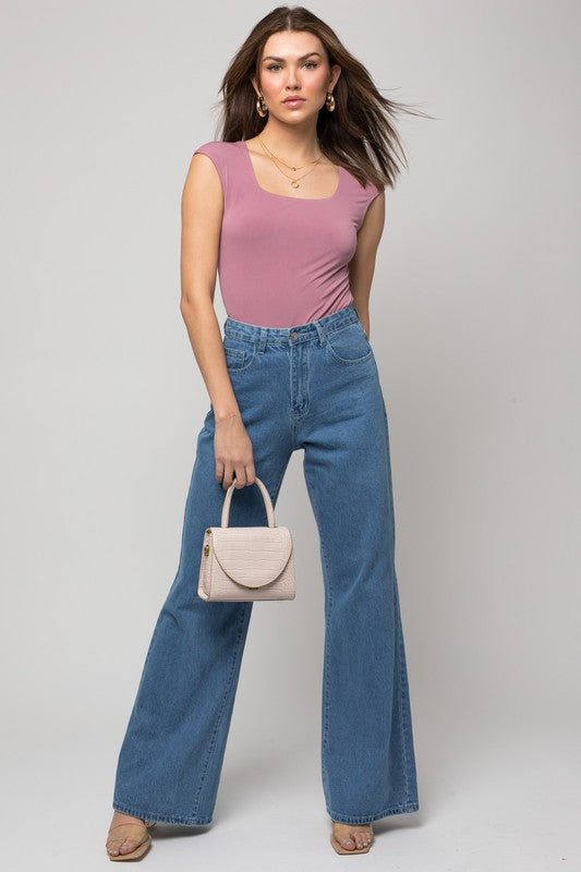 A person wearing a Cap Sleeve Square Neck Bodysuit and jeans holds a black handbag, showcasing a true fashion essential.