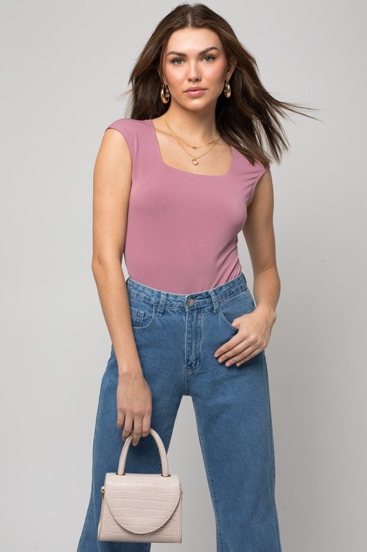 A person wearing a Cap Sleeve Square Neck Bodysuit and jeans holds a black handbag, showcasing a true fashion essential.