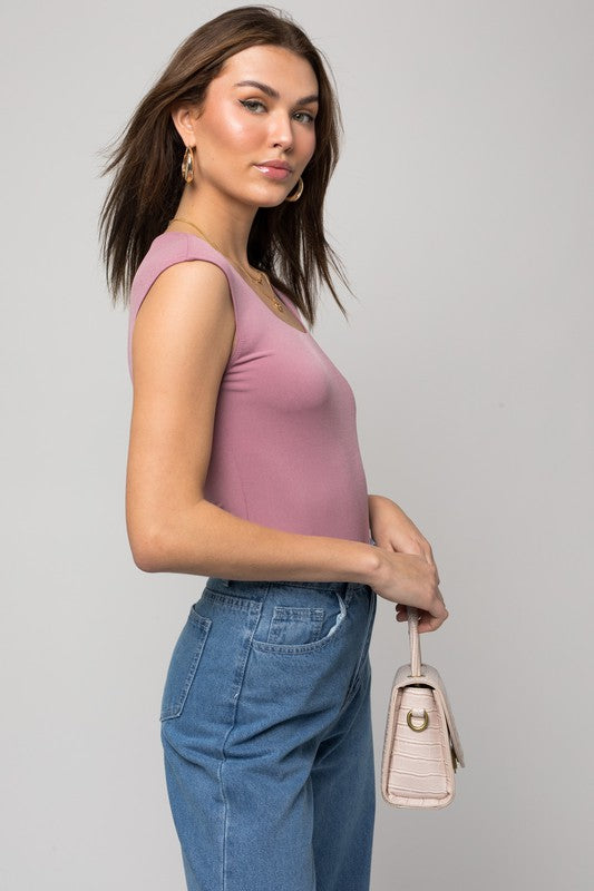 A person wearing a Cap Sleeve Square Neck Bodysuit and jeans holds a black handbag, showcasing a true fashion essential.