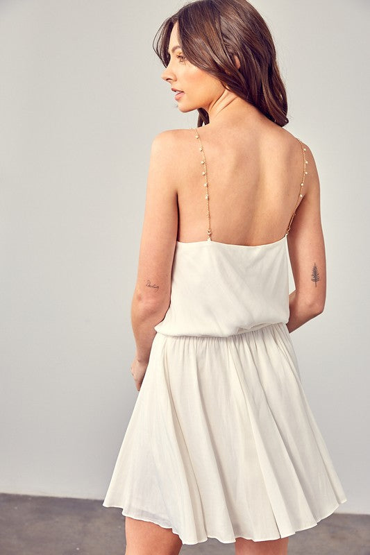 A woman wearing the Cowl Neck Beaded Strap Dress poses indoors against a simple backdrop, glancing to the side. Ideal for special occasions, this elegant piece is enhanced by its sleeveless design.