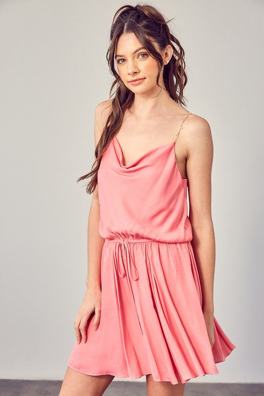 A woman wearing the Cowl Neck Beaded Strap Dress poses indoors against a simple backdrop, glancing to the side. Ideal for special occasions, this elegant piece is enhanced by its sleeveless design.