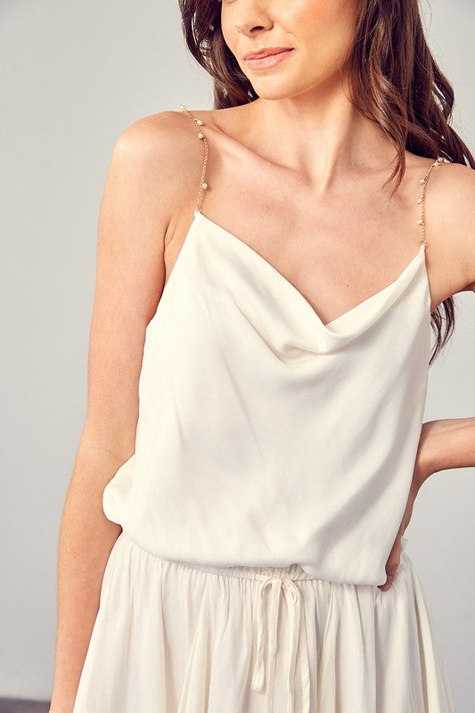 A woman wearing the Cowl Neck Beaded Strap Dress poses indoors against a simple backdrop, glancing to the side. Ideal for special occasions, this elegant piece is enhanced by its sleeveless design.