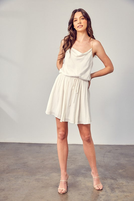 A woman wearing the Cowl Neck Beaded Strap Dress poses indoors against a simple backdrop, glancing to the side. Ideal for special occasions, this elegant piece is enhanced by its sleeveless design.