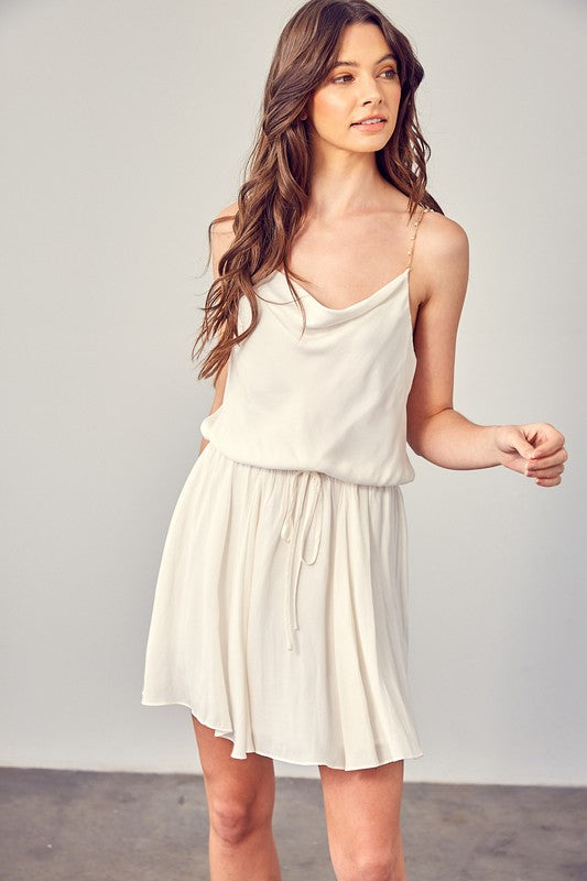 A woman wearing the Cowl Neck Beaded Strap Dress poses indoors against a simple backdrop, glancing to the side. Ideal for special occasions, this elegant piece is enhanced by its sleeveless design.