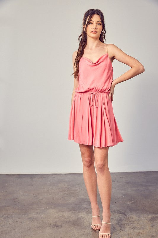 A woman wearing the Cowl Neck Beaded Strap Dress poses indoors against a simple backdrop, glancing to the side. Ideal for special occasions, this elegant piece is enhanced by its sleeveless design.