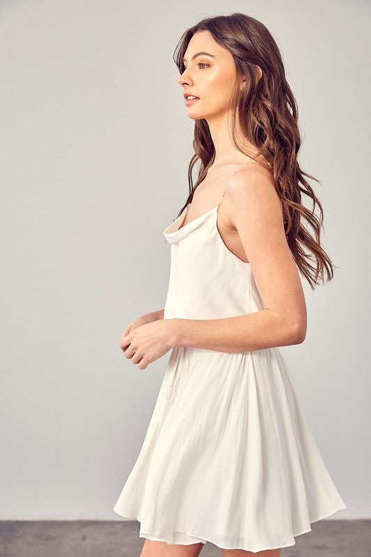 A woman wearing the Cowl Neck Beaded Strap Dress poses indoors against a simple backdrop, glancing to the side. Ideal for special occasions, this elegant piece is enhanced by its sleeveless design.