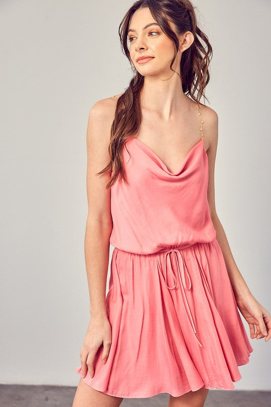 A woman wearing the Cowl Neck Beaded Strap Dress poses indoors against a simple backdrop, glancing to the side. Ideal for special occasions, this elegant piece is enhanced by its sleeveless design.