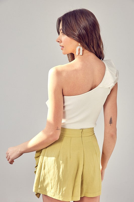 A woman dressed in a white One Shoulder Knit Top paired with a yellow skirt stands against a plain background.