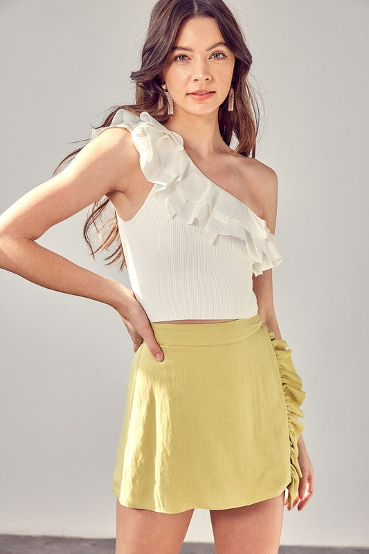 A woman dressed in a white One Shoulder Knit Top paired with a yellow skirt stands against a plain background.