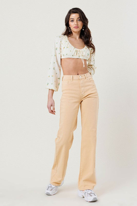 A person wearing a floral crop top, High Waisted Wide Cut Straight Leg Jeans crafted from organic cotton, and white sneakers stands against a plain background, effortlessly embodying sustainable fashion.