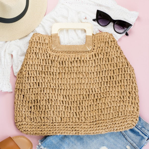 A person in a white tank top and denim shorts is holding an Oversized Straw Tote, featuring intricate woven details.