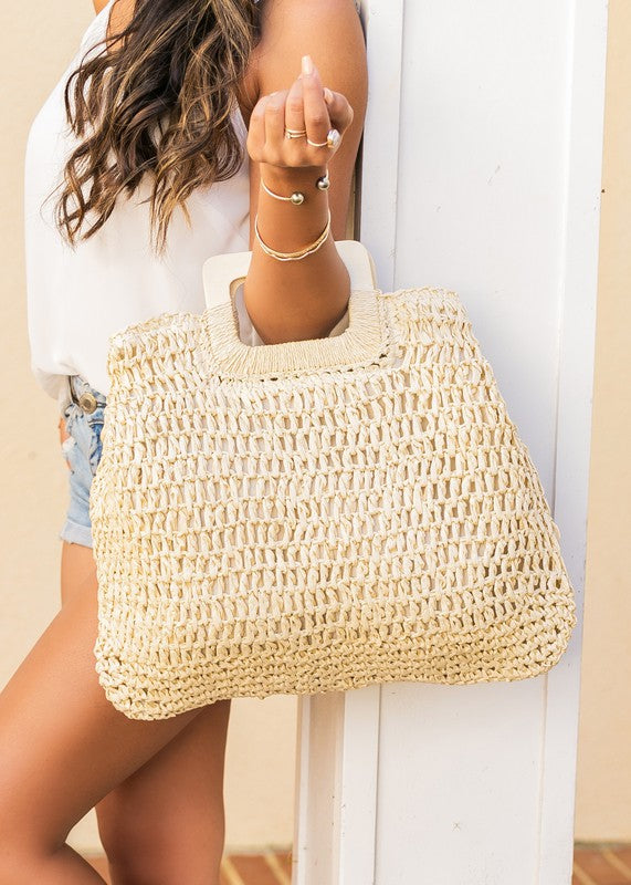 A person in a white tank top and denim shorts is holding an Oversized Straw Tote, featuring intricate woven details.