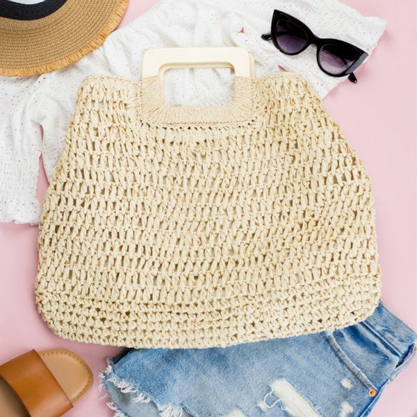 A person in a white tank top and denim shorts is holding an Oversized Straw Tote, featuring intricate woven details.