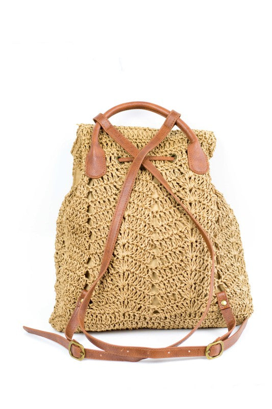 A person wearing a straw hat and white tank top carries the elegant Woven Straw Backpack, featuring charming PU leather straps.