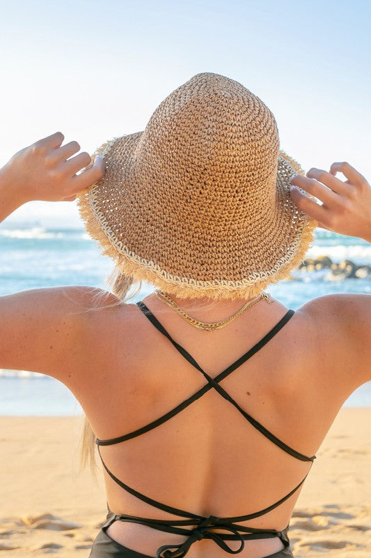 Woman wearing a Frayed Edge Straw Bucket Hat and sunglasses at the beach.