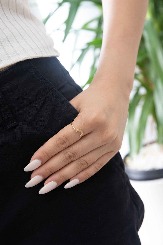 The All Smiles Ring showcases a sleek, minimalistic design characterized by its elegant curved v-shape and finished with a luxurious 14k gold plating. It is embellished with delicate round gemstones and beautifully presented against a white background.