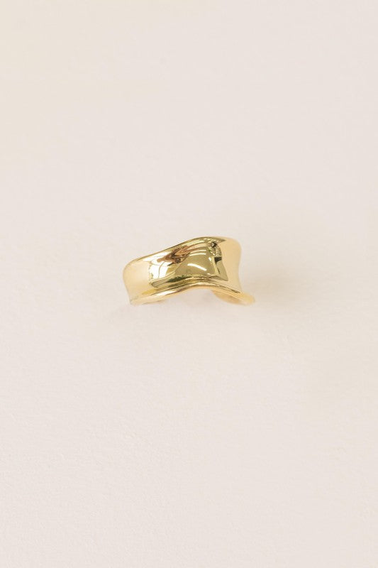 The Sculpted Adjustable Ring, plated in 14k gold with a smooth, shiny finish, is elegantly displayed on a light, textured background.