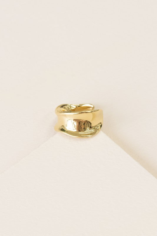 The Sculpted Adjustable Ring, plated in 14k gold with a smooth, shiny finish, is elegantly displayed on a light, textured background.