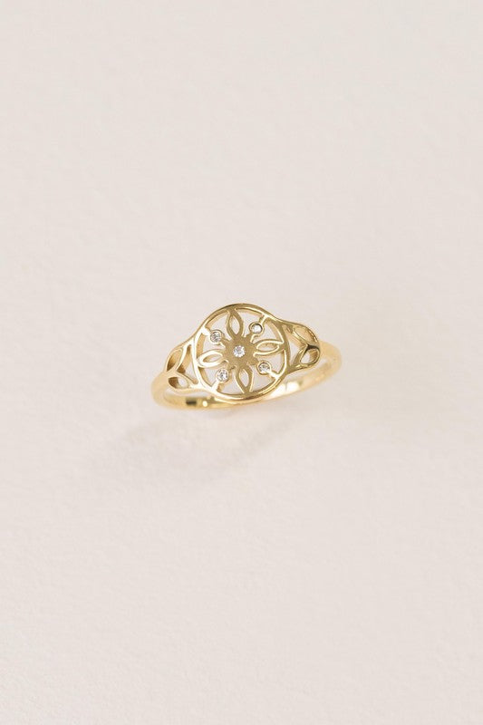 The Dreamer Ring boasts a sunburst design adorned with a small central gem, beautifully set against a textured off-white background. With its 14k gold-plated finish, this ring captivates with timeless elegance.