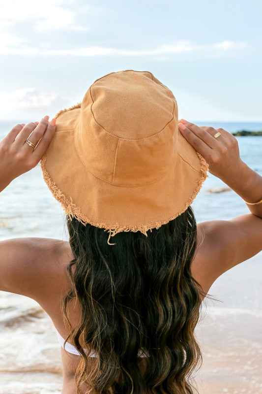 Woman in a white swimsuit and Frayed Edge Canvas Bucket Hat at the beach looking into the distance.