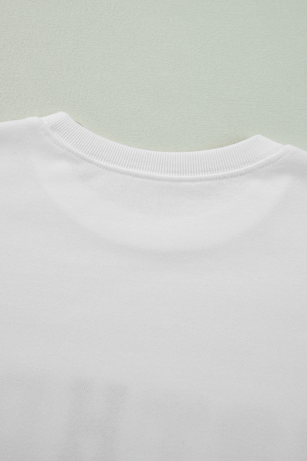 A person with long blonde hair is wearing a White BIRTHDAY QUEEN Graphic Balloon Sleeve Sweatshirt, paired with a pink feathered skirt, and sitting against a beautifully decorated backdrop.