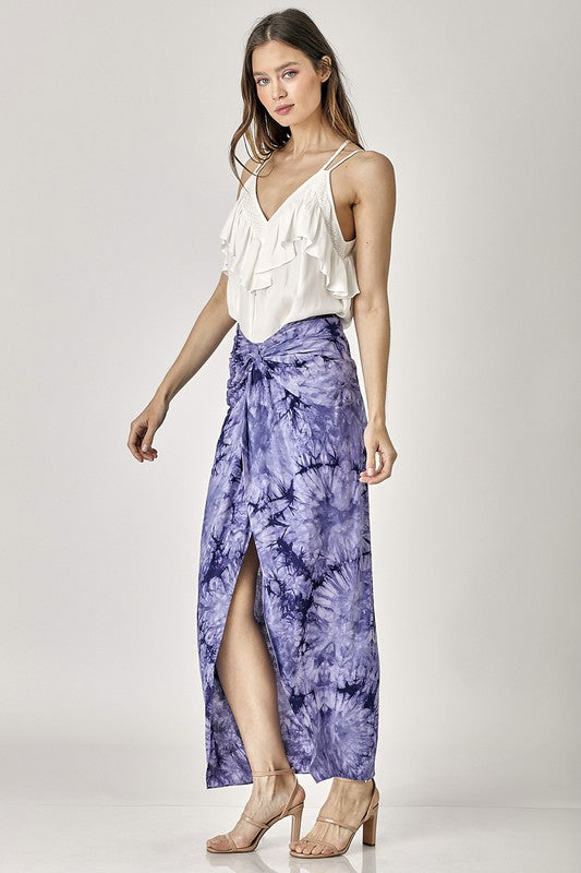 A woman wearing a white Trim Detail with Ruffle Cami Top paired with a purple tie-dye skirt poses against a plain background—an ideal choice for enhancing your summer wardrobe.