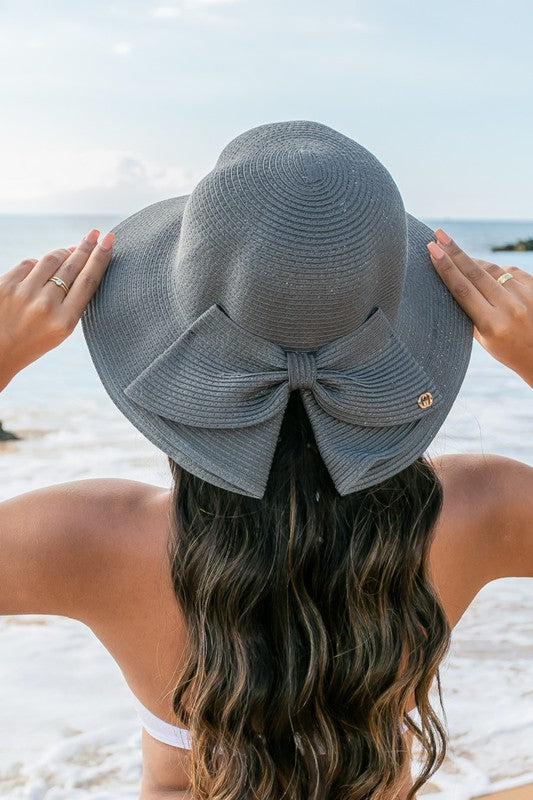 A person holding onto a Bow Back Straw Bucket Hat at the beach.