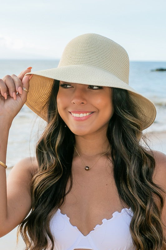 A person holding onto a Bow Back Straw Bucket Hat at the beach.