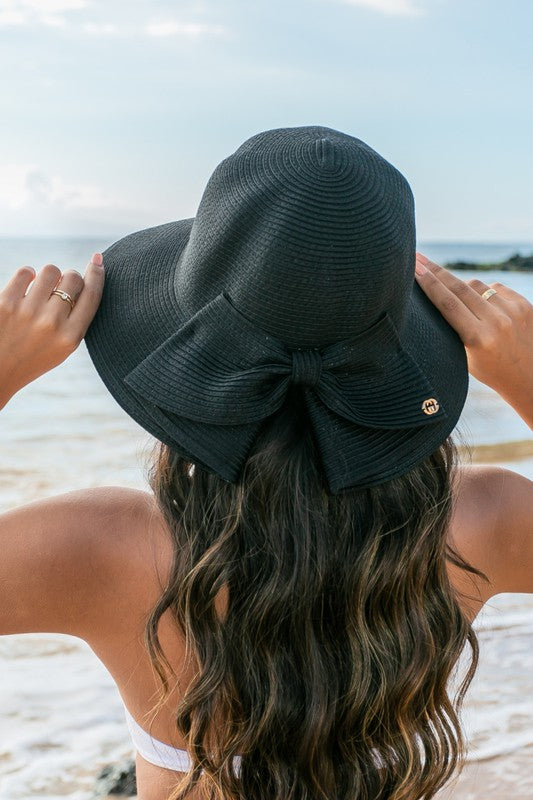 A person holding onto a Bow Back Straw Bucket Hat at the beach.