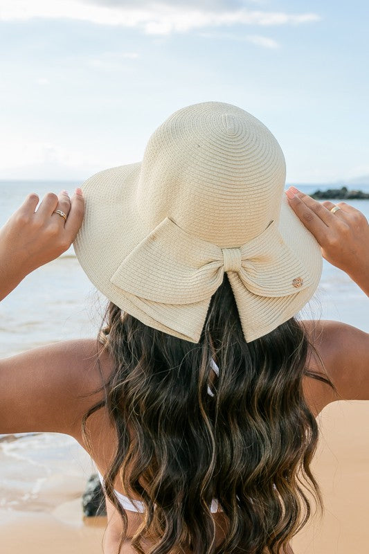 A person holding onto a Bow Back Straw Bucket Hat at the beach.