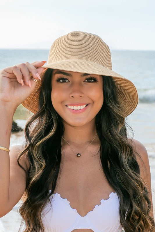 A person holding onto a Bow Back Straw Bucket Hat at the beach.