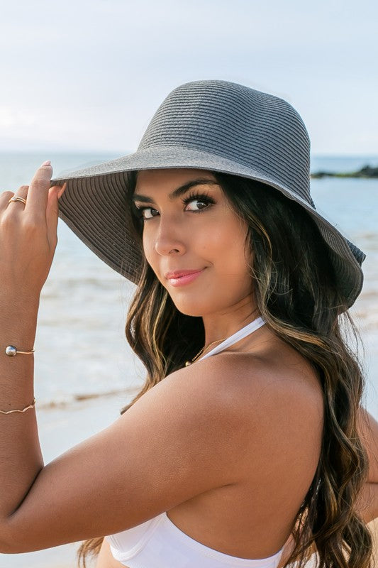 A person holding onto a Bow Back Straw Bucket Hat at the beach.